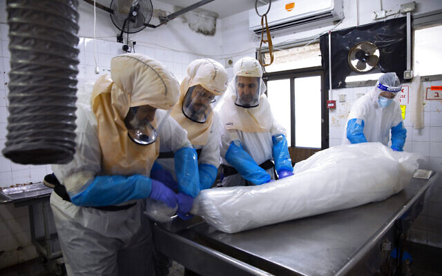 Workers prepare a body before a funeral procession at a special morgue for people who died from COVID-19 in the central Israeli city of Holon, near Tel Aviv, January 10, 2021. (AP Photo/Oded Balilty)