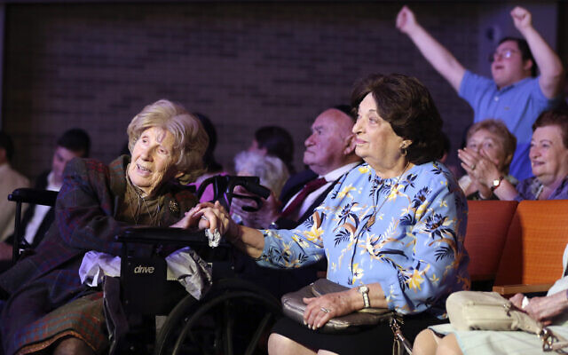Aranka Engel, 103, left, holds the hand of fellow Holocaust survivor Jean Kurz, 81, while watching Orthodox Jewish singer Yaakov Shwekey perform at a concert honoring them and dozens of other Holocaust survivors on Monday, June 14, 2021, at the Yeshivah of Flatbush theater at Joel Braverman High School in the Brooklyn borough of New York. It was the first large gathering for New York-area Holocaust survivors after more than a year of isolation due to the coronavirus pandemic. (AP Photo/Jessie Wardarski)