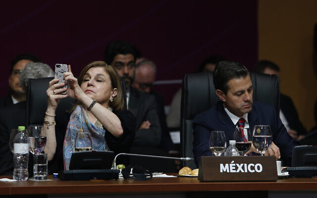 Mexico's then-president Enrique Pena Nieto takes notes as an unidentified Mexican diplomat takes pictures with her mobile phone during the plenary session at the Americas Summit in Lima, Peru, Saturday, April 14, 2018. (AP/Karel Navarro)