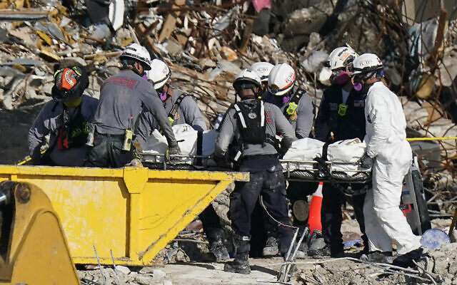 Search and rescue personnel remove remains on a stretcher as they work atop the rubble at the Champlain Towers South condo building where scores of people remain missing more than a week after it partially collapsed, Friday, July 2, 2021, in Surfside, Fla. Rescue efforts resumed Thursday evening after being halted for most of the day over concerns about the stability of the remaining structure.(AP Photo/Mark Humphrey)