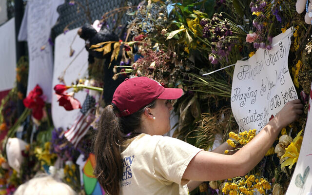 Molly MacDonald, with Mercy Chefs, hangs a sign on behalf of Princeton Church at a makeshift memorial remembering the victims of the nearby collapsed Champlain Towers South building on July 14, 2021, in Surfside, Fla. (AP Photo/Lynne Sladky)