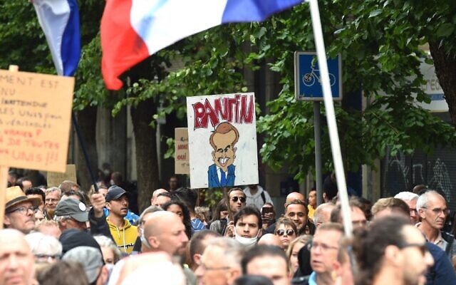 Illustrative -- A protester holds a banner depicting French President Emmanuel Macron as a 'puppet' during a demonstration, part of a national day of protest against the mandatory COVID-19 health pass to access most of the public space, in Lille, northern France, on August 7, 2021. (Francois Lo Presti/AFP)