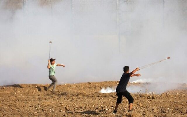 Palestinians use slingshots to hurl rocks at Israeli security forces across the Gaza border during a demonstration by the fence with Israel, east of Gaza City on August 21, 2021. (Photo by SAID KHATIB / AFP)