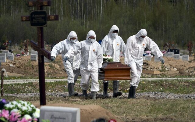 Gravediggers in protective suits carry the coffin of the deceased, who died of COVID-19, as relatives and friends stand at a distance in the coronavirus section of a cemetery in Kolpino, outside St. Petersburg.  (AP Photo/Dmitri Lovetsky, File)