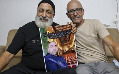 Malek Hassuna (L) carries a picture of his late son Mussa, who was shot dead on May 10, as he sits with Effi Yehoshua, brother of Yigal Yehoshua, killed on May 11, in Lod on August 18, 2021. (Ahmad Gharabli/AFP)