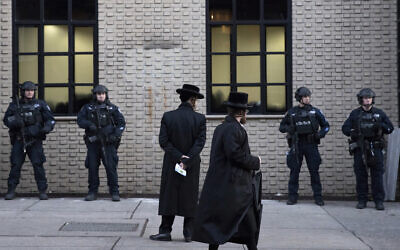 In this illustrative photo from December 11, 2019, Orthodox Jewish men pass by New York City police guarding a Brooklyn synagogue prior to a funeral for Mosche Deutsch, a rabbinical student from Brooklyn who was killed in a shooting at a Jersey City, New Jersey market. (AP Photo/Mark Lennihan, File)