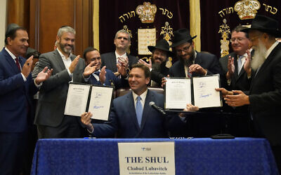 Surrounded by state legislators and Jewish leaders, Florida Gov. Ron DeSantis, center, holds up two bills that he signed on June 14, 2021, at The Shul of Bal Harbour, a Jewish community center in Surfside, Florida. (AP Photo/Wilfredo Lee)