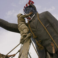Cpl. Edward Chin of the US 3rd Battalion, 4th Marines Regiment, covers the face of a statue of Saddam Hussein with an American flag before toppling the statue in downtown Baghdad, Iraq, April 9, 2003. (Jerome Delay/AP)