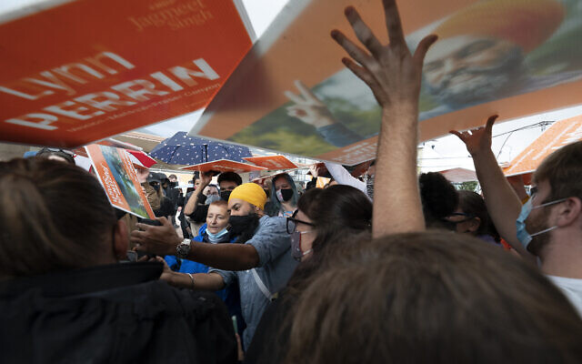 New Democratic Party supporters use signs as rain shields, as NDP Leader Jagmeet Singh greets people during a campaign stop in Pitt Meadows, British Columbia, on Sunday, September 19, 2021. (Jonathan Hayward/The Canadian Press via AP)