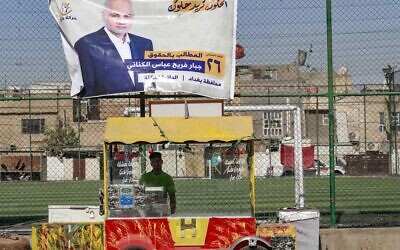An Iraqi street vendor stands beneath an electoral billboard of a candidate for the upcoming parliamentary elections, in the capital Baghdad's Sadr City neighborhood, on October 9, 2021. (AHMAD AL-RUBAYE / AFP)