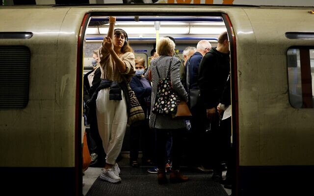 Commuters, some wearing face masks to help prevent the spread of coronavirus, wait for an underground train to leave from a station in central London, on October 19, 2021. (Tolga Akmen/AFP)