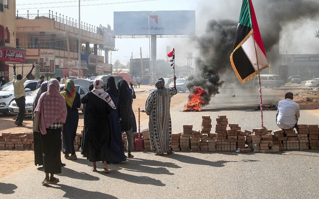 Sudanese protesters lift national flags next to a brick roadblock during a demonstration in the capital Khartoum, on October 25, 2021, to denounce overnight detentions by the army of members of Sudan's government. (Photo by AFP)