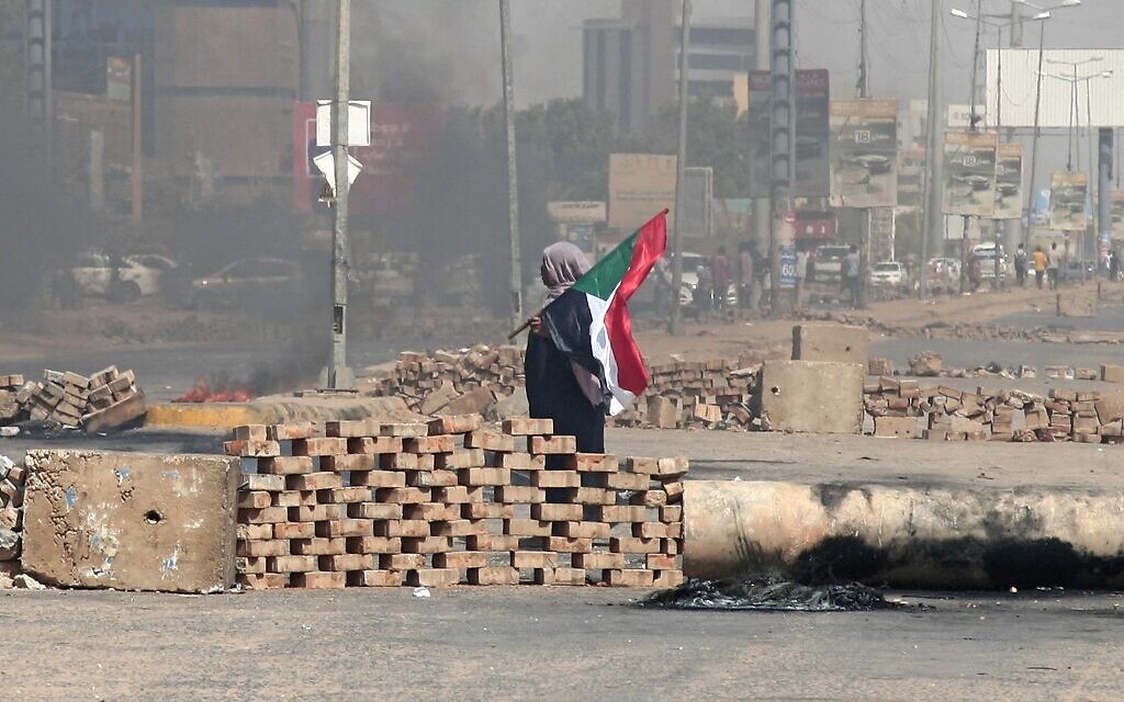 A Sudanese demonstrator carrying a national flag walks by roadblocks set up by protesters on a street in the capital Khartoum, on October 26, 2021. (AFP)