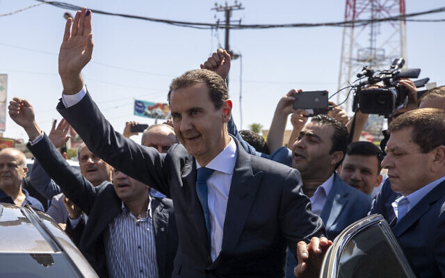 In this May 26, 2021 file photo, Syrian President Bashar Assad, center, waves to his supporters at a polling station during the Presidential elections in Douma, Syria. (AP Photo/Hassan Ammar)