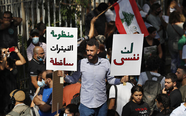 A protester holds Arabic placards that reads: 'Will not forget, right, down with the system of nitrates,' outside a court building during a demonstration of solidarity with Judge Tarek Bitar who is investigating last year's deadly seaport blast, in Beirut, Lebanon, Wednesday, September 29, 2021. (AP Photo/Hussein Malla)