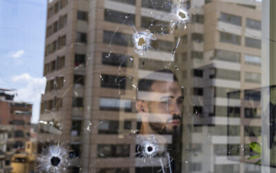 An employee looks through an office window riddled with bullet holes after the deadly clashes that erupted a week earlier along a former 1975-90 civil war front-line between Muslim Shiite and Christian areas, in Ain el-Rumaneh neighborhood, Beirut, Lebanon, October 19, 2021. (AP Photo/Hassan Ammar)