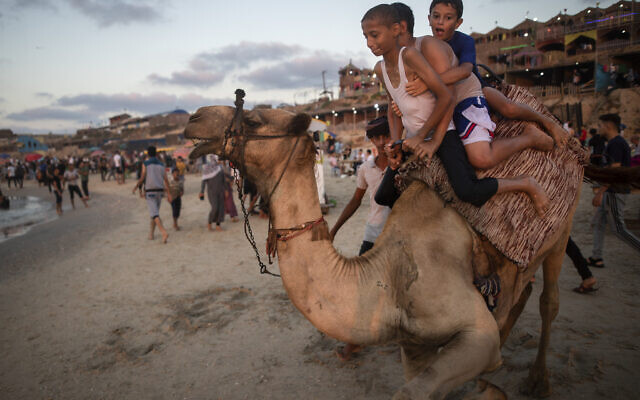 Palestinian children react as they ride a camel on the beach of Gaza City,Aug. 20, 2021. (AP Photo/Khalil Hamra)