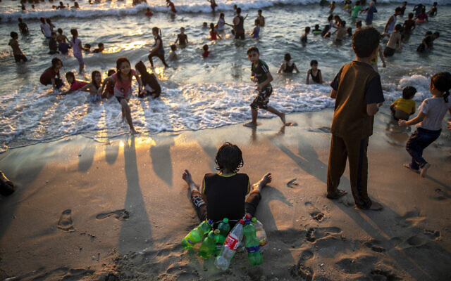 A Palestinian boy uses empty plastic bottles to flood while swimming, rests on the beach of Gaza City, July 9, 2021. (AP Photo/Khalil Hamra)