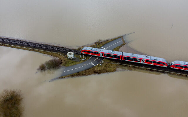 A train passes a railroad crossing surrounded by floodwaters from rain and melting snow in Nidderau near Frankfurt, Germany, on February 3, 2021. (AP Photo/Michael Probst)