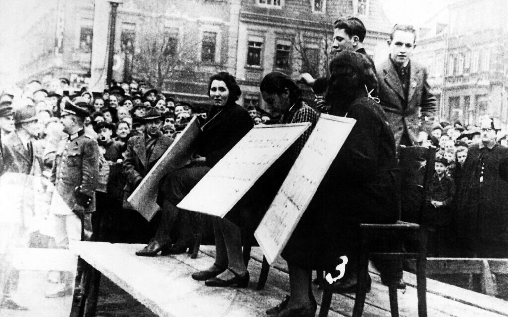 After the Kristallnacht pogrom in Linz, Austria, Jewish women are made to wear signs saying, 'I am not part of the national community,' while being humiliated on stage in public (public domain)
