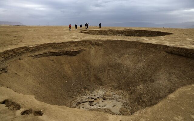 Hikers walk next to sinkholes across a dried-up sea area which exposed and created a salt plain, some 20 kilometers south of Kibbutz Ein Gedi in the southern part of the Dead Sea, on January 15, 2021. (Menahem KAHANA / AFP)