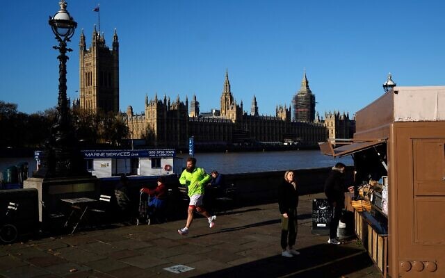 A jogger runs past the Palace of Westminster, comprising the House of Lords and the House of Commons, on the banks of the River Thames in London on November 22, 2021 (Niklas Halle'n/AFP)