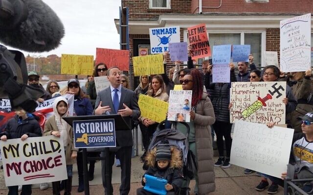 A protester, right, holds up a sign with a swastika during an anti-vaccine protest outside the Bronx office of Assemblyman Jeffrey Dinowitz, November 14, 2021. Former Westchester County executive and gubernatorial candidate Rob Astorino, at podium, spoke at the rally. (courtesy, Jeffrey Dinowitz, via Twitter)