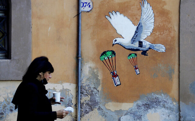 A woman walks past a mural depicting a white dove parachuting COVID-19 vaccine vials, posted near the Italian Health Ministry Headquarters in Rome, April 4, 2021. (AP/Gregorio Borgia, file)