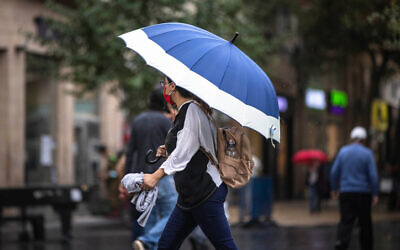 People take cover from the rain as they walk on Jaffa Road  in the city center of Jerusalem on October 31, 2021 (Olivier Fitoussi/Flash90)