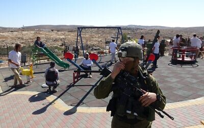 An Israeli soldier stands by as Israeli settlers enter a Palestinian playground in Susiya, a Palestinian hamlet in the West Bank, on Saturday, November 6, 2021 (Credit: Guy Butuvia)