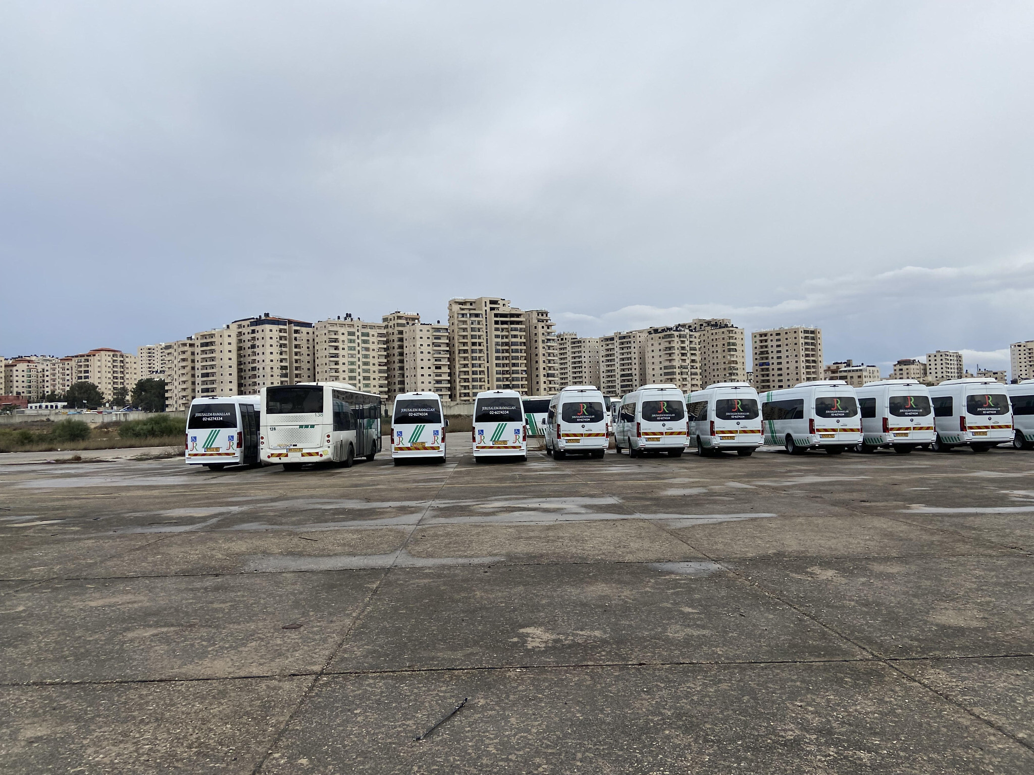 Buses parked at what was once Jerusalem Airport at Atarot; in the background, the high-rises of the Kafr Aqab neighborhood -- formally part of Jerusalem but outside the security barrier, November 2021. (David Horovitz / Times of Israel)