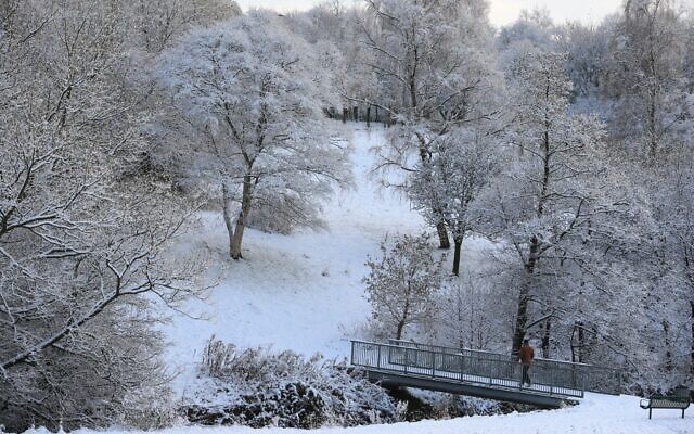 A walker crosses a bridge in snowy conditions in Brun Valley Forest Park in Burnley, north-west England on November 28, 2021, as the north of England recovers from the after effects of Storm Arwen. (Lindsey Parnaby / AFP)