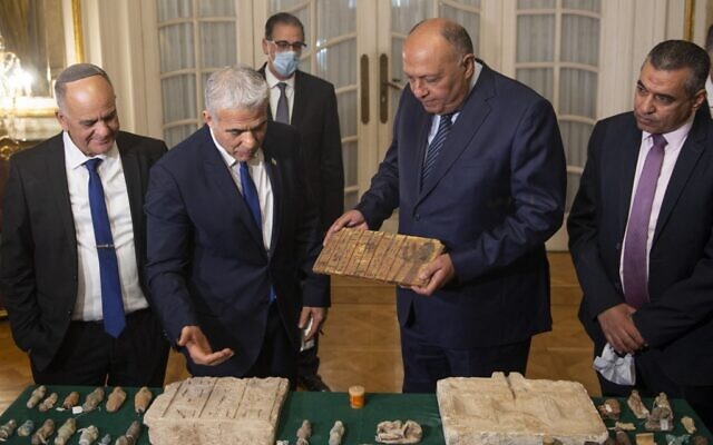 Israel Antiquities Authority Director Eli Escozido (L) looks on as Israeli Foreign Minister Yair Lapid (C-L) presents Egypt's Foreign Minister Sameh Shoukry (C-R) with stolen Egyptian artifacts that were smuggled to Israel and returned back to Egypt, during their meeting at Tahrir Palace in Cairo on December 9, 2021. (Mohamed HOSSAM / AFP)
