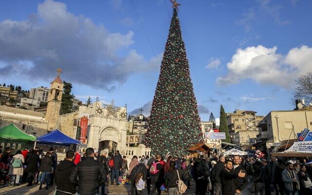 People gather around the giant Christmas tree outside the Greek Orthodox Church of the Annunciation in Israel's northern city of Nazareth on December 18, 2021. (AHMAD GHARABLI / AFP)