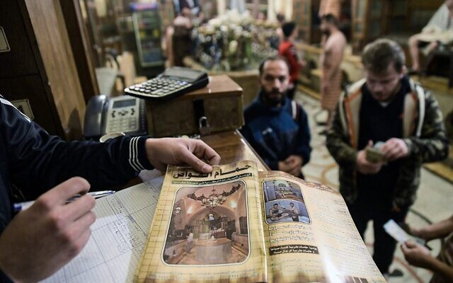 A worker presents the facility pamphlet at the entrance of Hammam al-Qawas, a traditional Turkish bathhouse, in Syria's northern city of Aleppo on December 16, 2021. (Photo by AFP)