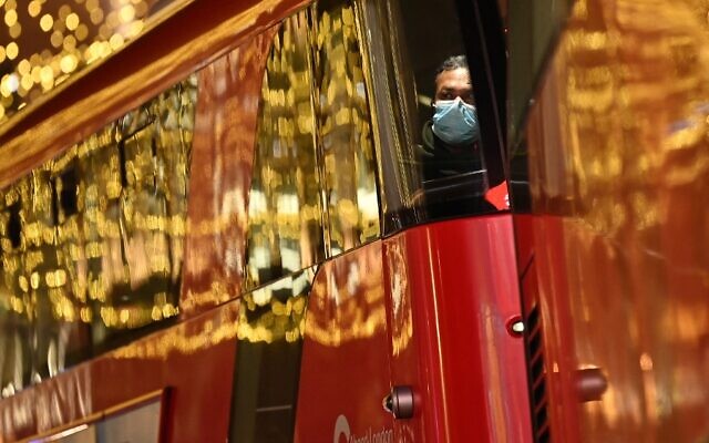 A passenger wearing a face covering to combat the spread of COVID-19 sits on a red double-decker bus traveling beneath Christmas lights in London on December 21, 2021. (Justin Tallis/AFP)