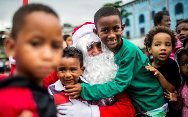 A man dressed as Santa Claus hugs children during a Christmas meal distribution a favela in Rio de Janeiro, Brazil, on December 23, 2021 (Daniel Ramalho/AFP)