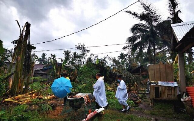 This photo taken on December 24, 2021, Roman Catholic priest Fr. Ricardo Virtudazo (center) walking among toppled banana trees caused by Super Typhoon Rai, as he visits typhoon-affected parishioners in Alegria, Surigao del Norte province.(Ferdinandh Cabrera/AFP)