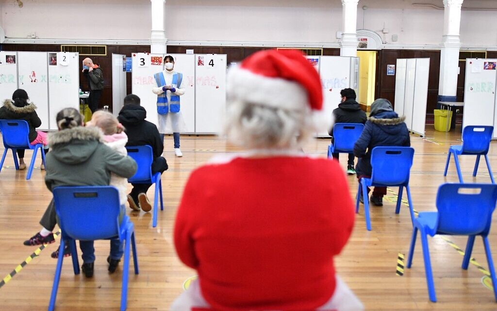 A volunteer looks on as people wait to receive a dose of the COVID19 vaccine at a pop-up coronavirus vaccination centre at the Redbridge Town Hall, east London on December 25, 2021 (JUSTIN TALLIS / AFP)