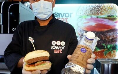 A man holds a cut half of a plant-based patty, made and cooked by a robot according to customer requirements, offered by Israeli fast food brand BBB in Herzliya on December 28, 2021.  (Photo by JACK GUEZ / AFP)