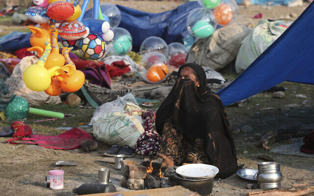 An Indian migrant worker, who makes her living by selling balloons and toys, cooks food for her family outside a tent on a cold morning in a slum in Jammu, India, Dec. 23, 2020. (AP Photo/Channi Anand)