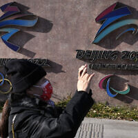 A woman wearing takes photos near the logos for the Beijing Winter Olympics and Paralympics in Beijing, China, Nov. 9, 2021 (AP Photo/Ng Han Guan)