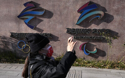 A woman wearing takes photos near the logos for the Beijing Winter Olympics and Paralympics in Beijing, China, Nov. 9, 2021 (AP Photo/Ng Han Guan)