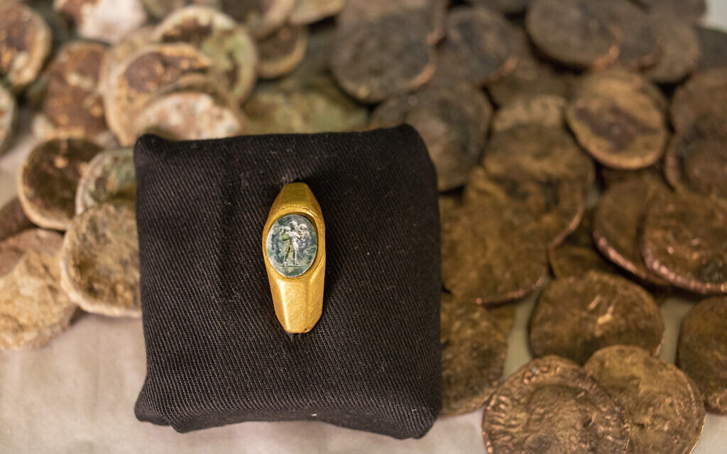 Foreground: A recently discovered gold ring with a green gemstone carved with the figure of the Good Shepherd. Background: A hoard of coins from the Mamluk period recently discovered in a shipwreck off the coast of Caesarea. (AP Photo/Ariel Schalit)