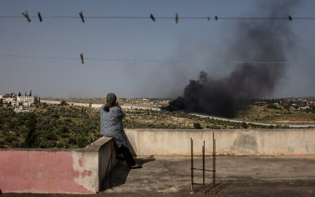 Maysoon Sweity, a 54-year-old Palestinian from Beit Awwa, sits on the roof of her home and watches as e-waste and garbage burns near the concrete wall separating her village from Israel on April 26, 2019. (Tamir Kalifa)