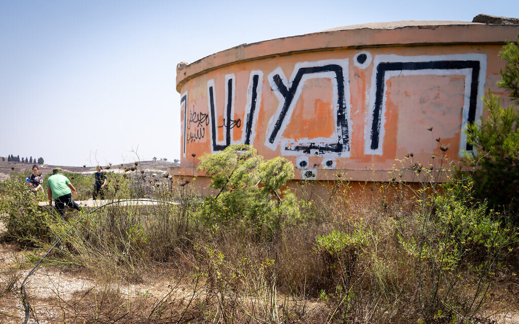 People walk by the water tower on the ruins of Homesh, August 27, 2019. (Hillel Meir/Flash90)