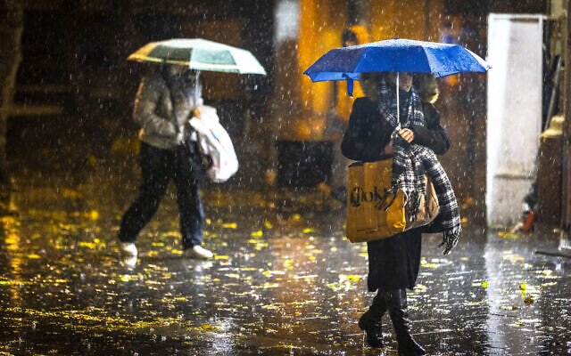 People take cover from the rain as they walk on Jaffa Road in the city center of Jerusalem on December 20, 2021. (Olivier Fitoussi/Flash90)