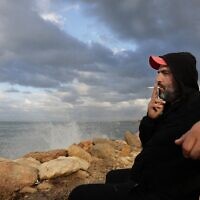 Lebanese would-be-migrant Bilal Moussa, 34, smokes a cigarette by the sea in Tripoli north of Beirut on December 9, 2021. (JOSEPH EID / AFP)