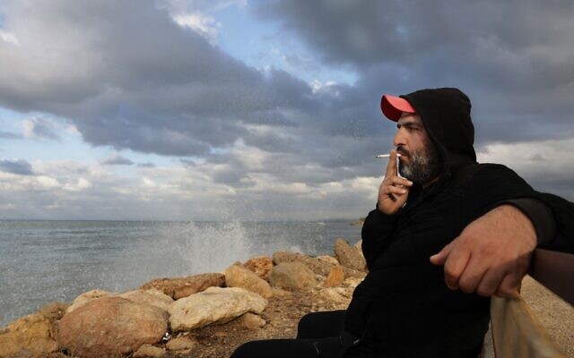 Lebanese would-be-migrant Bilal Moussa, 34, smokes a cigarette by the sea in Tripoli north of Beirut on December 9, 2021. (JOSEPH EID / AFP)