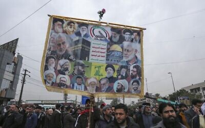 A man lifts an anti-US and anti-Israel placard as members and supporters of Iraq's al-Hashed al-Shaabi ex-paramilitary alliance take part in a demonstration and a symbolic funeral for Qasem Soleimani and Abu Mahdi al-Muhandis in Baghdad, on January 1, 2022. (Sabah Arar/AFP)